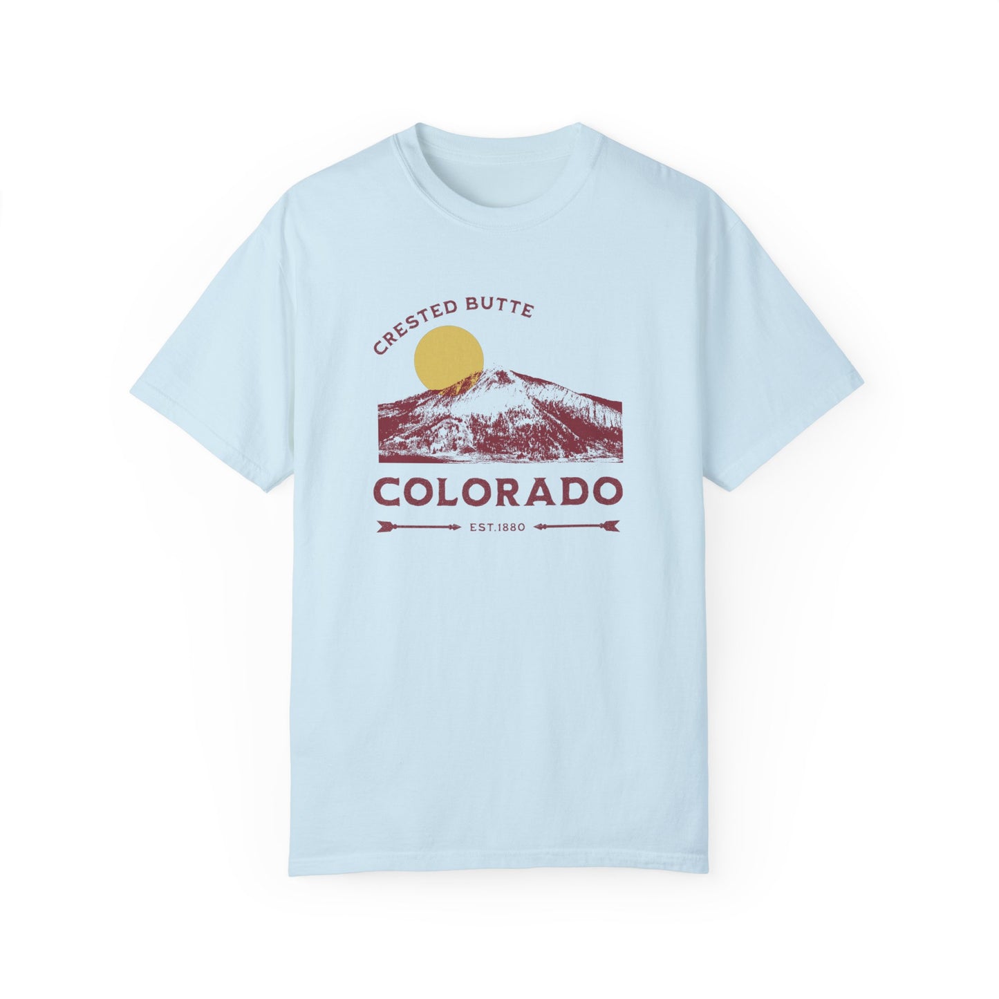 A light blue T-shirt with a graphic print of a mountain range and the text 'Crested Butte Colorado'. The design gives off a vintage vibe with a ski mountain backdrop.