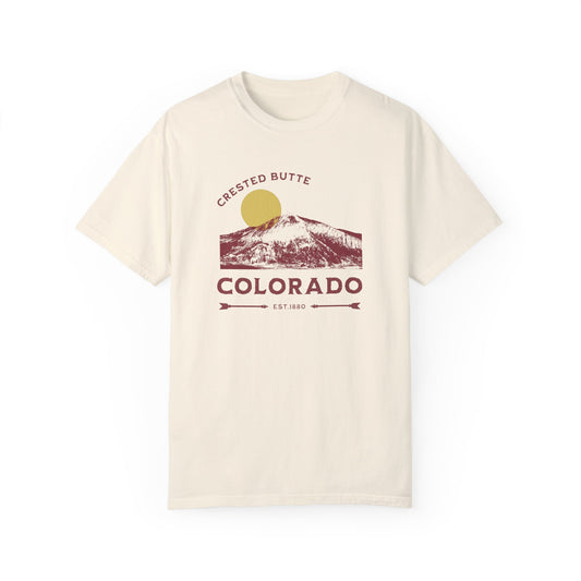 A beige t-shirt with a graphic illustration of Mt. Crested Butte and the text 'CRESTED BUTTE COLORADO' on the front.