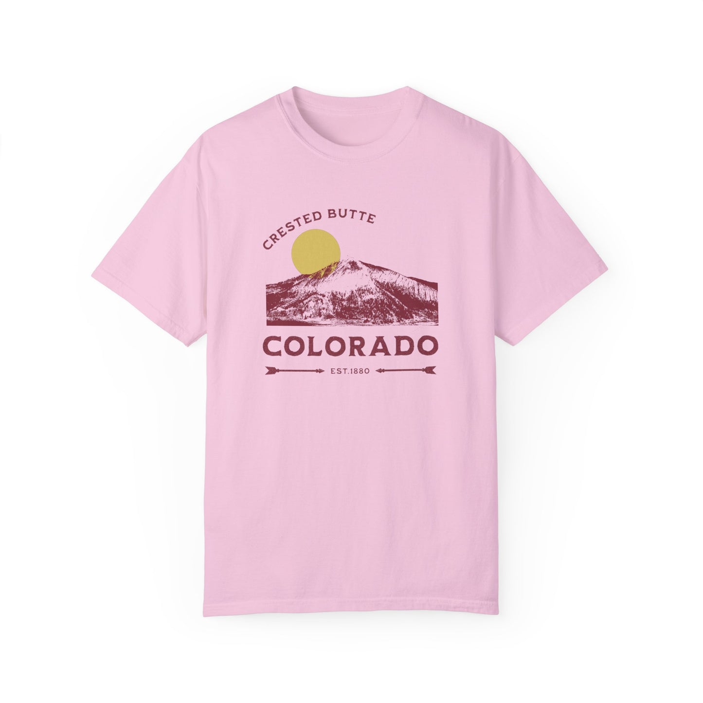 A pink t-shirt with a graphic print of a mountain range and the text 'Crested Butte Colorado'. The design includes a stylized sun motif.