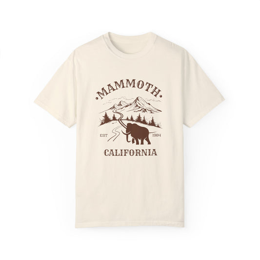 A beige t-shirt featuring a mammoth silhouette with a ski mountain backdrop and the text 'MAMMOTH CALIFORNIA'.