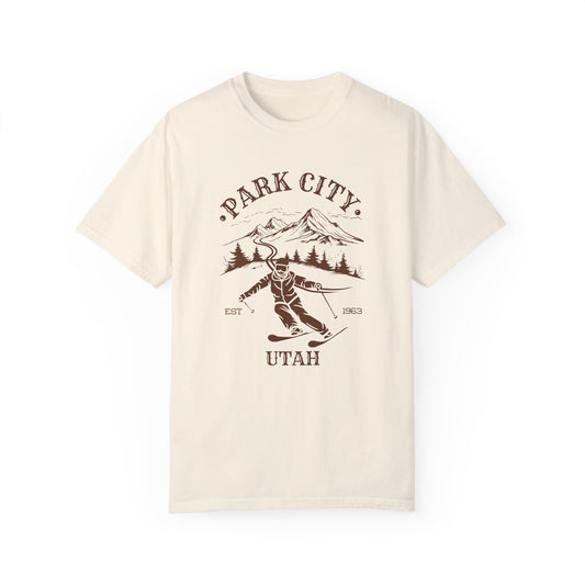 A beige t-shirt featuring a skier silhouette with a ski mountain backdrop and the text 'PARK CITY UTAH'.